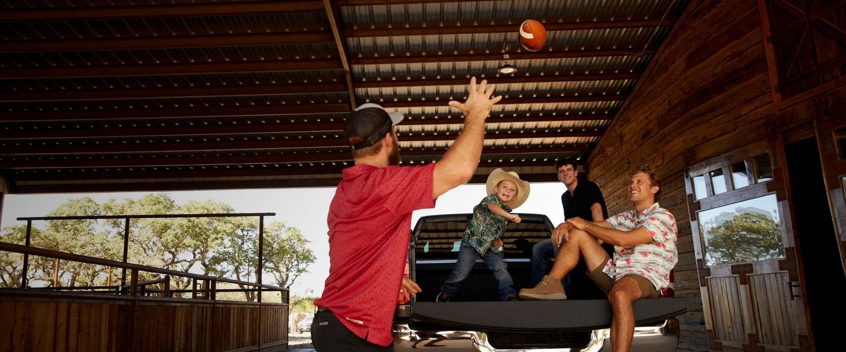 man playing catch with kids sitting in the back of a pick up truck
